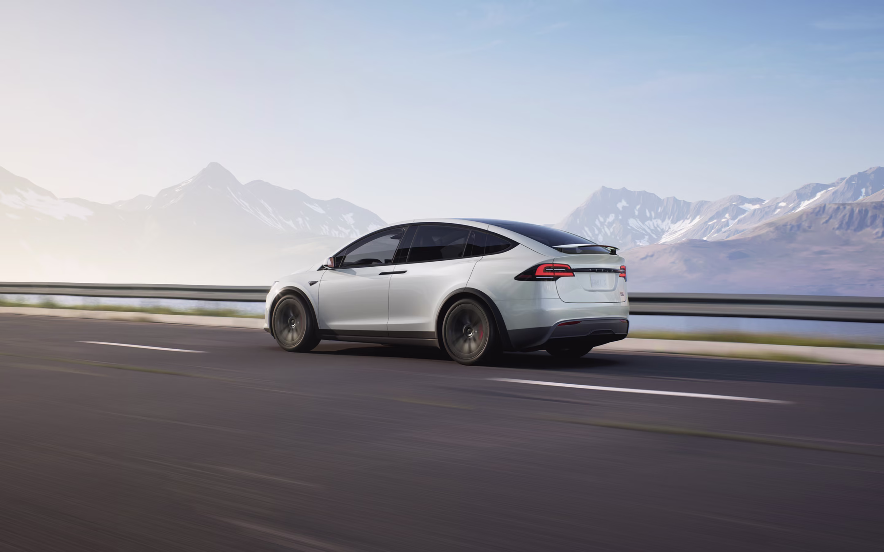 Red Model 3 driving down a lakeside road